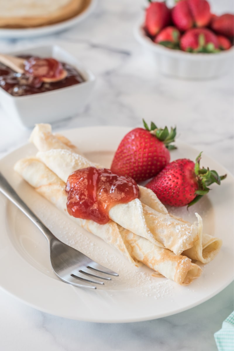 norwegian pancakes topped with strawberry jam with fresh strawberries