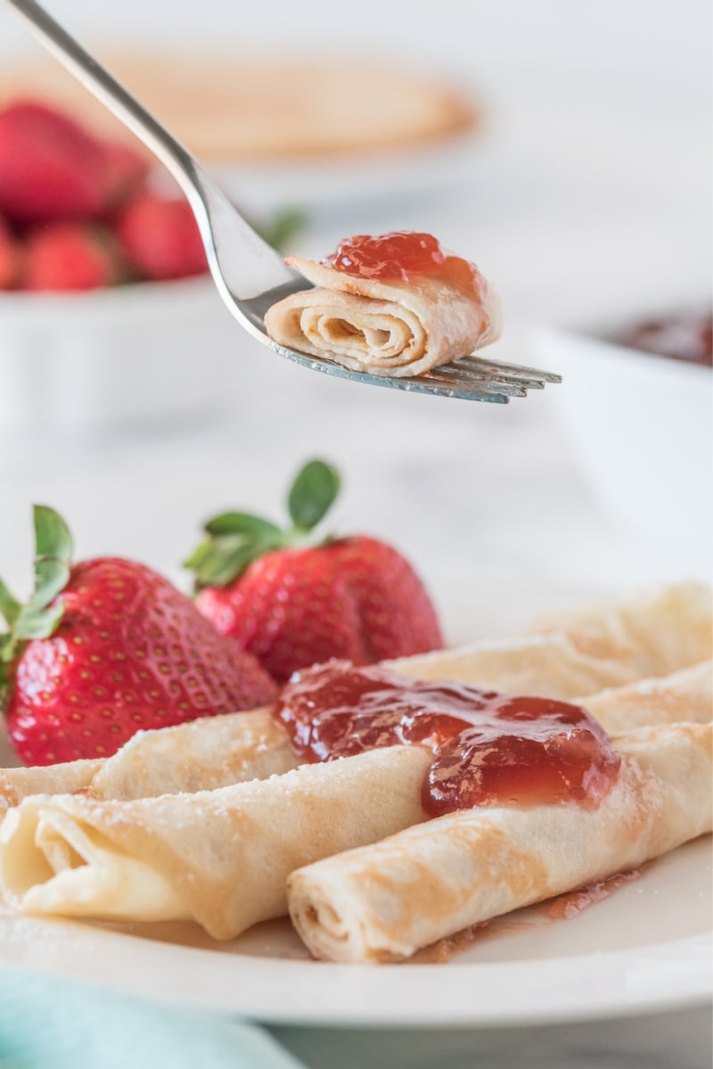 fork full of pancakes over plate of norwegian pancakes topped with strawberry jam with fresh strawberries