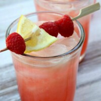 two glasses of spiked raspberry lemonade with a toothpick garnish of raspberries and lemon on top