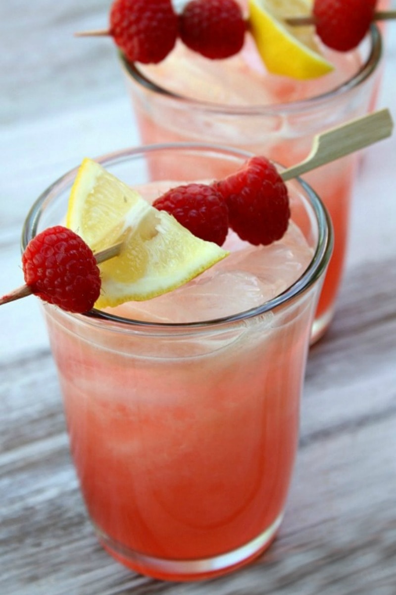 two glasses of spiked raspberry lemonade with a toothpick garnish of raspberries and lemon on top