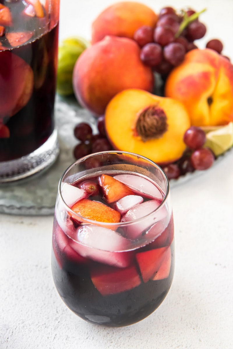 glass of red wine sangria with pitcher in the background and grapes and peaches