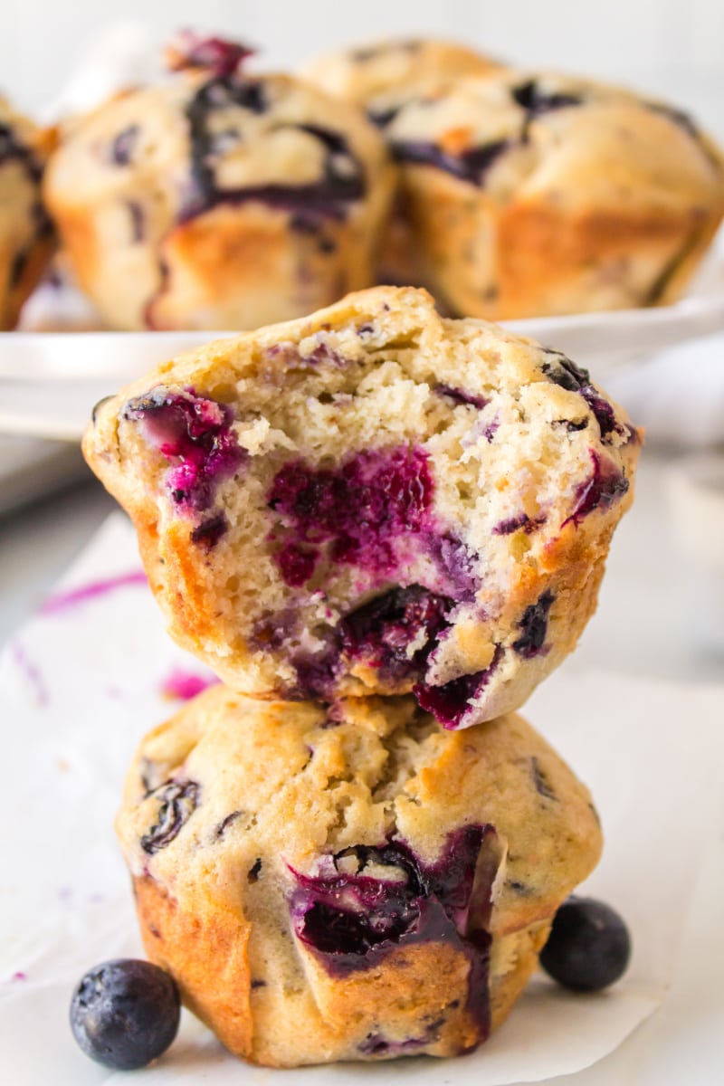 two blueberry muffins stacked one with bite out of it