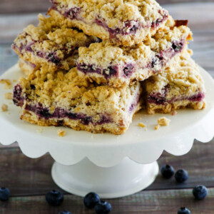 lemon blueberry streusel bars stacked on a white display platter with a wood background