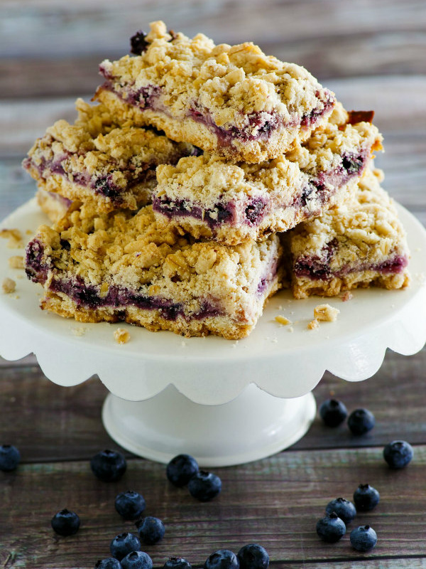 lemon blueberry streusel bars stacked on a white display platter with a wood background