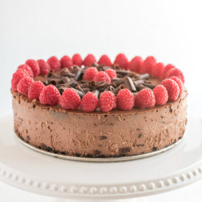 chocolate chocolate chip cheesecake with raspberry garnish on white platter