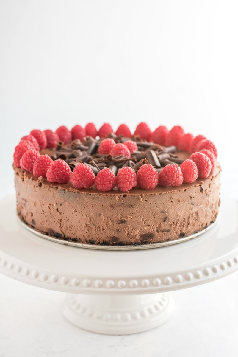 chocolate chocolate chip cheesecake with raspberry garnish on white platter