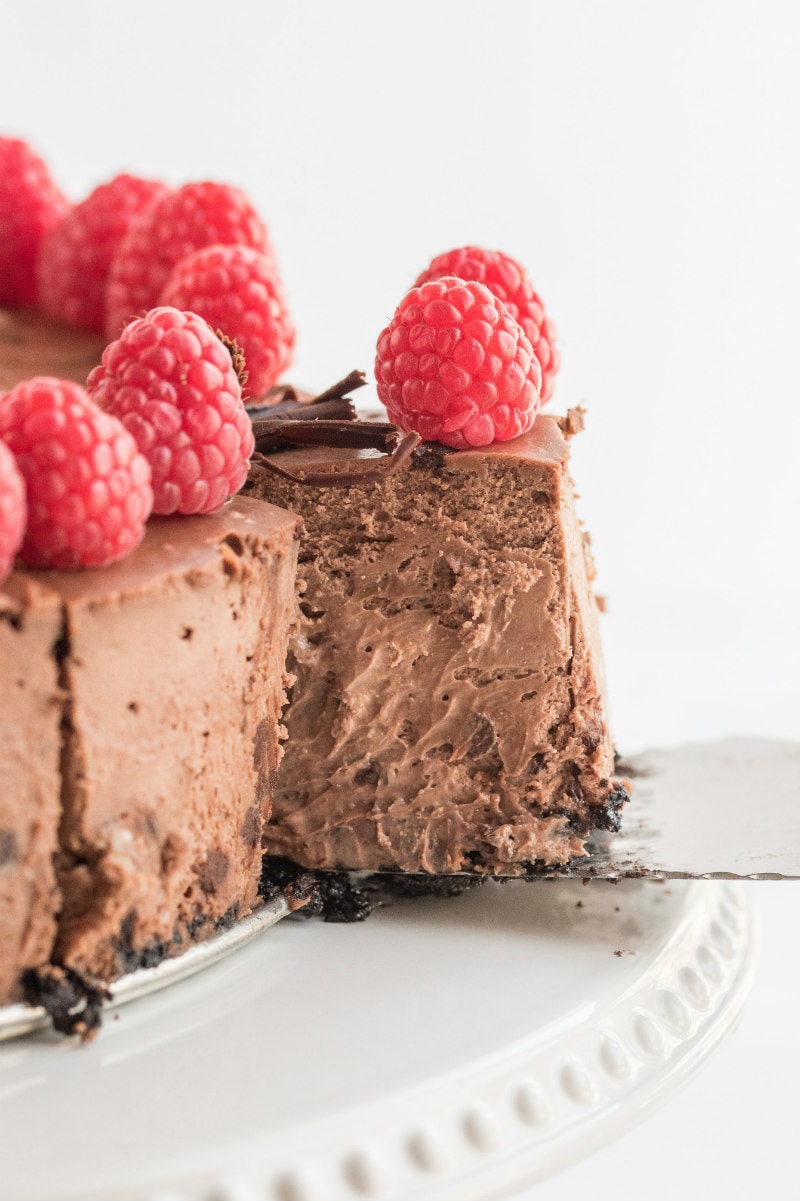 spatula removing slice of chocolate cheesecake from the cake on white platter