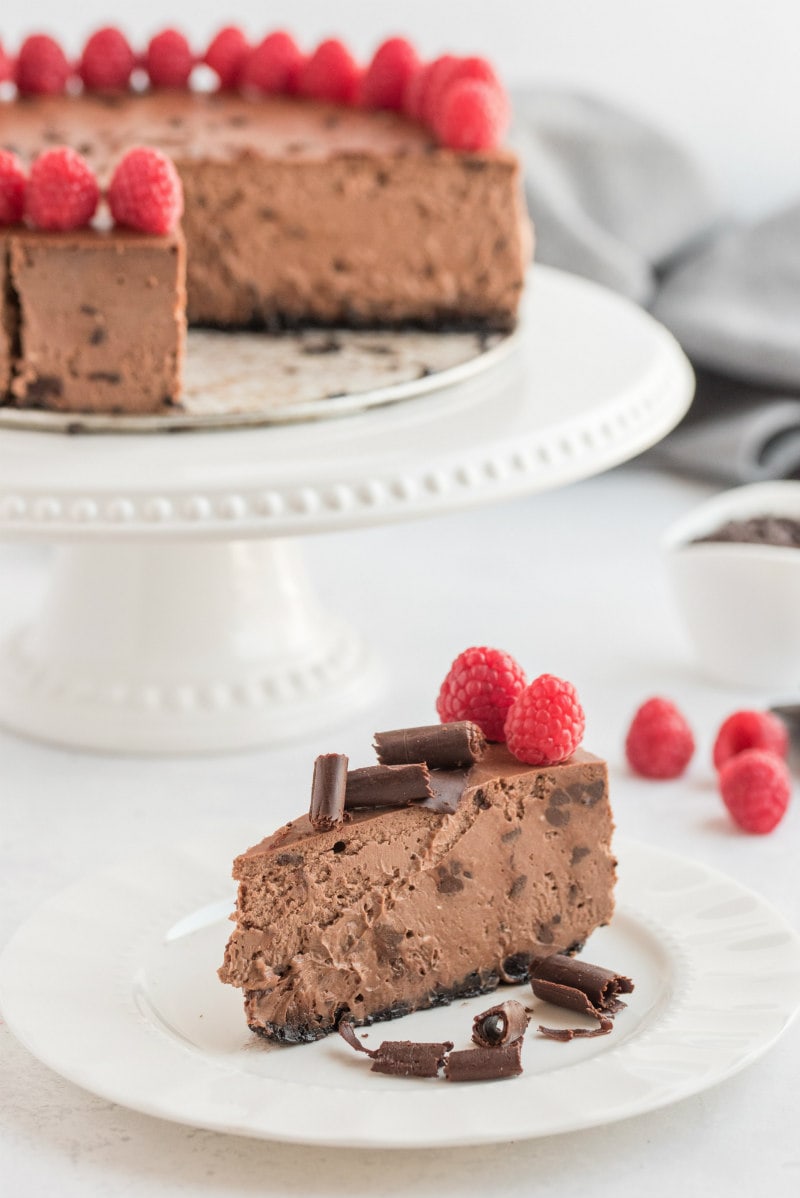 slice of chocolate cheesecake on white plate with rest of cheesecake in background