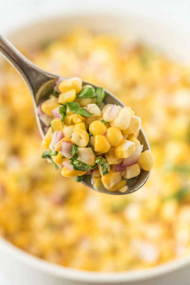 spoonful of fresh corn salad above a white bowl of corn salad