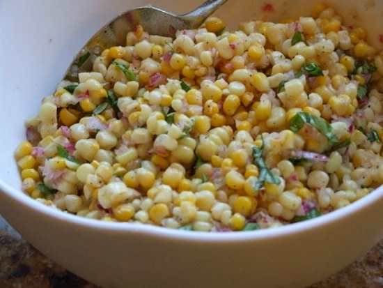 Fresh Corn Salad in a white serving bowl with a serving spoon