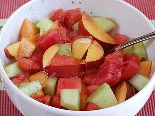 fruit salad in a white bowl with a spoon