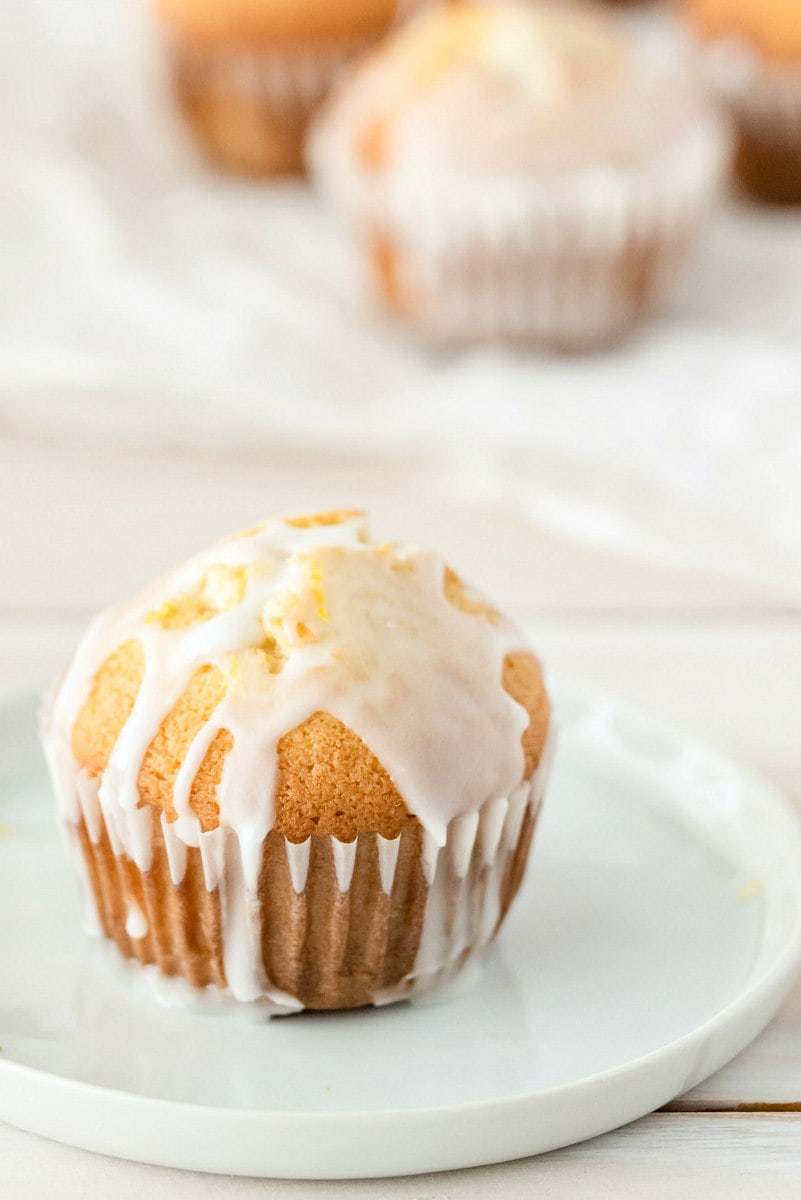 lemon pound cake muffin with glaze sitting on a white plate with more muffins in the background