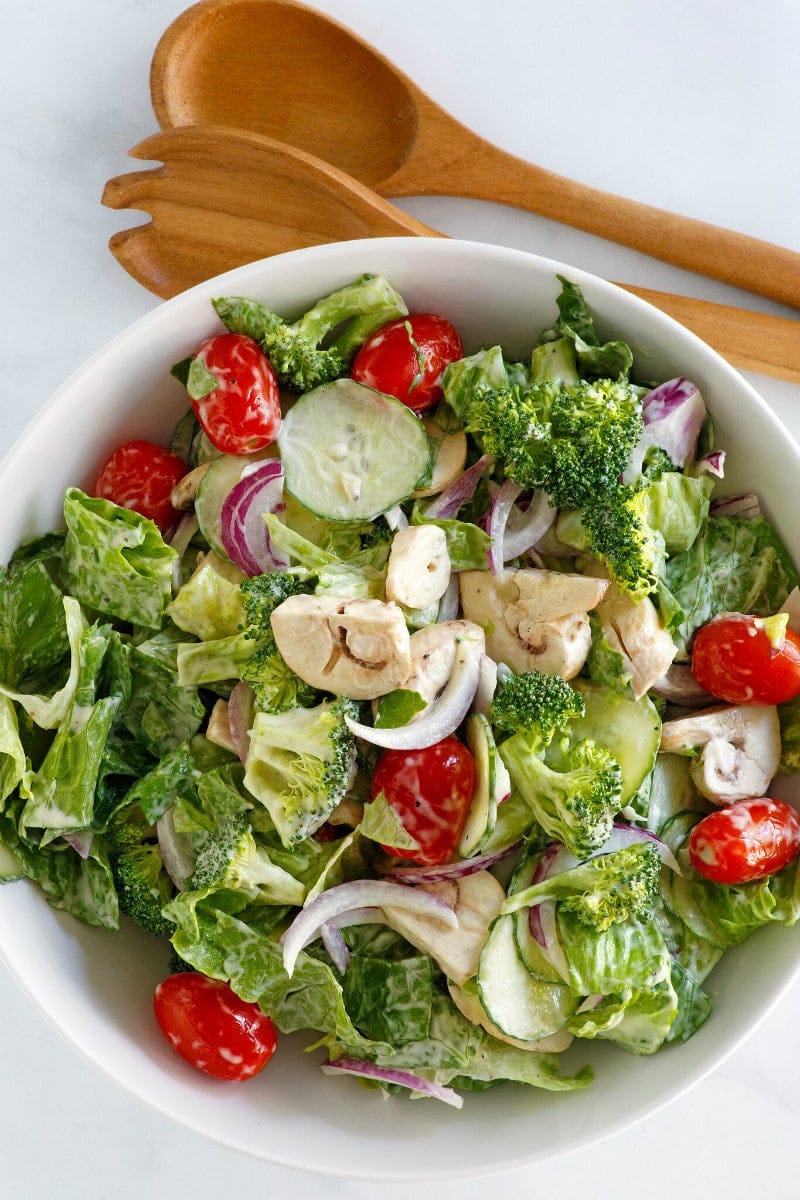 White Bowl of Romaine and Broccoli Salad with wooden utensils in the background