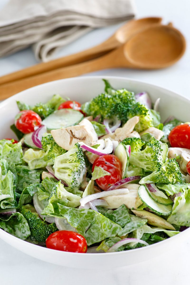 White bowl of Romaine and Broccoli Salad with wooden serving utensils in the background