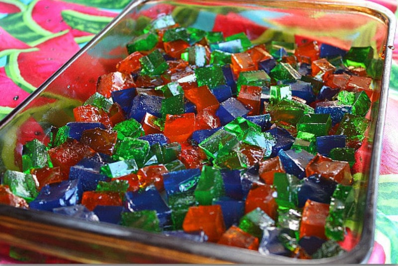 chopped up pieces of different colors of jello in a pyrex pan