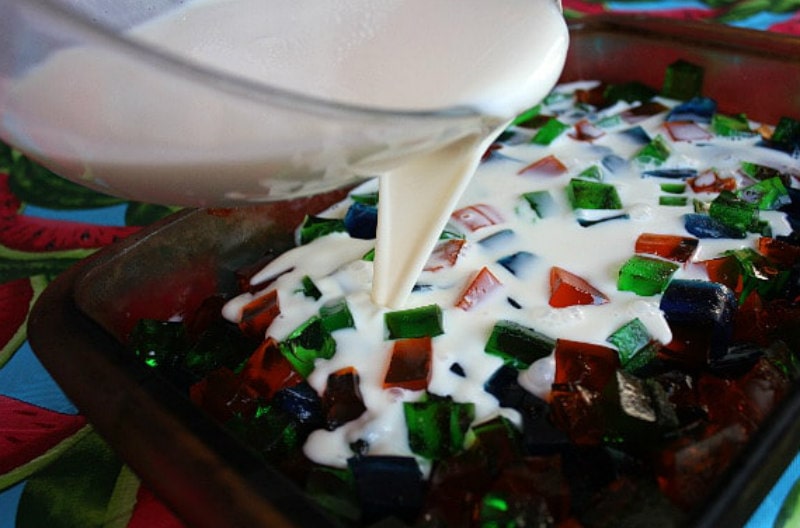 pouring sweet white jello mixture onto pieces of colored jello in a pan