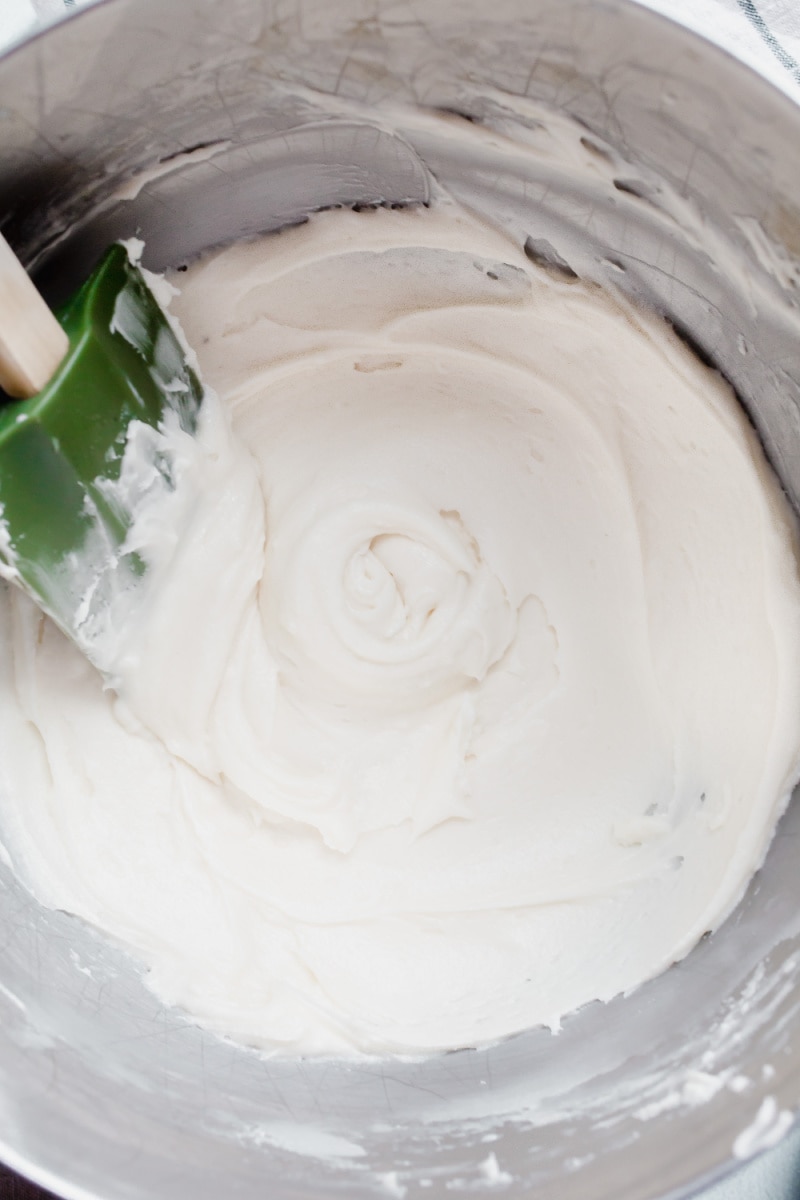 White frosting in bowl with green rubber spatula