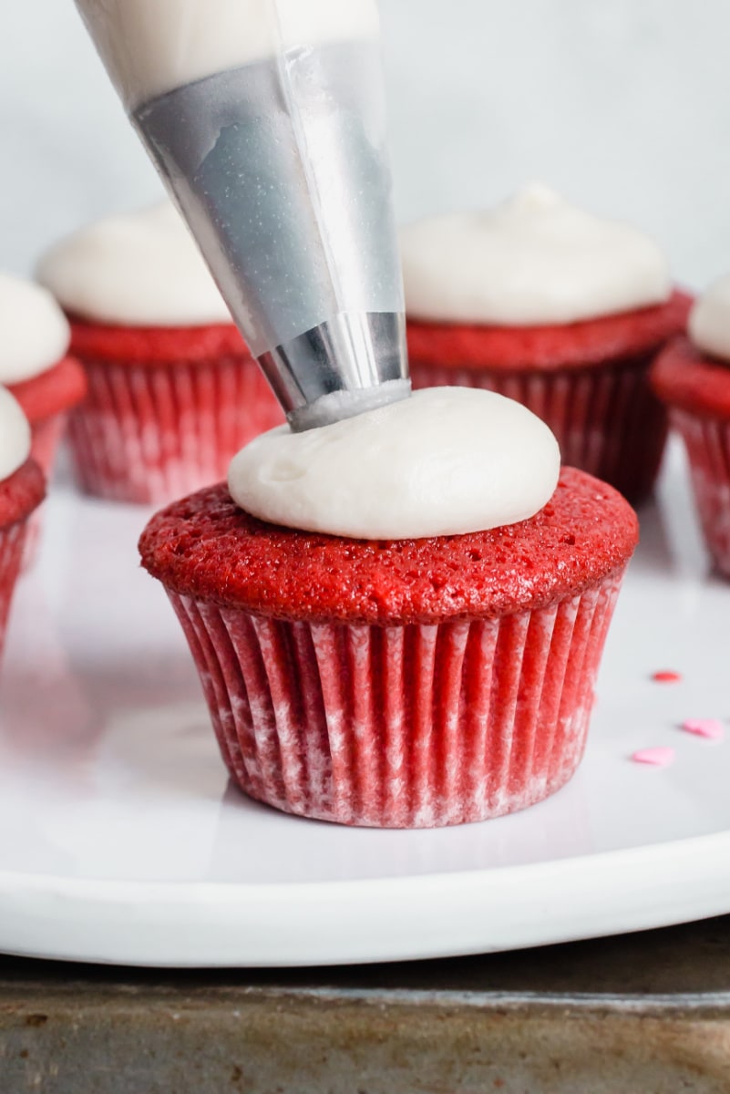 Piping frosting onto red velvet cupcake