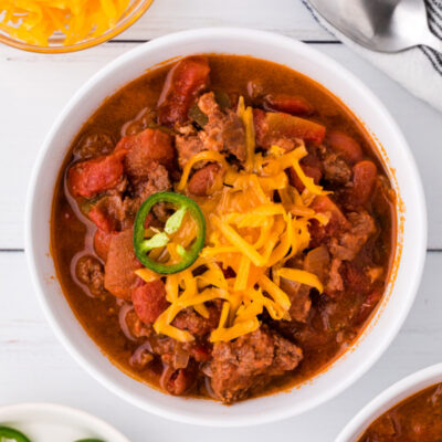 white bowl of chili topped with cheese and jalapeno