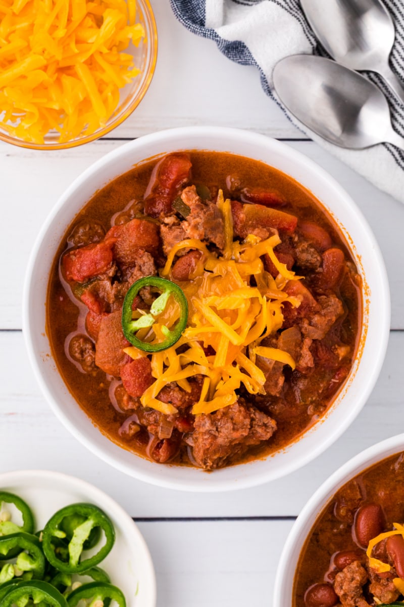 white bowl of chili topped with cheese and jalapeno