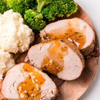 slices of pork roast topped with apricot glaze on plate with potato and broccoli