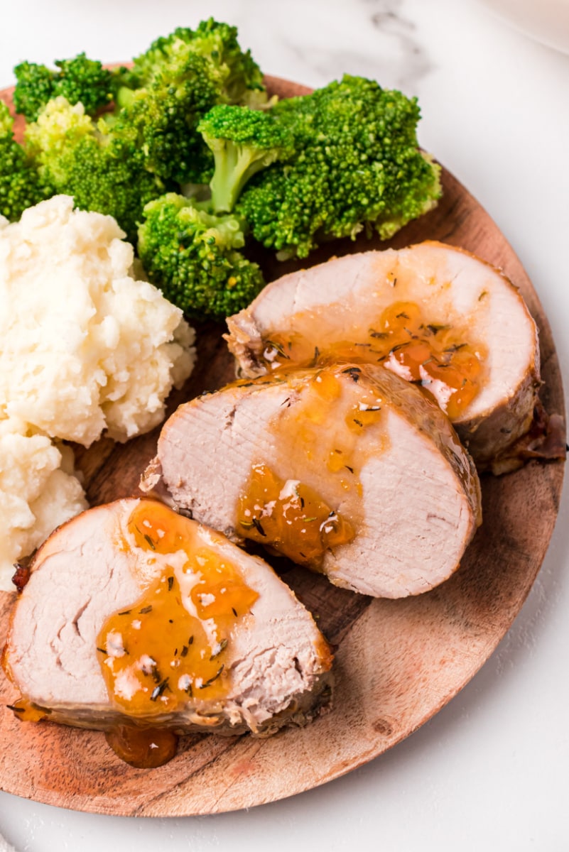 slices of pork roast topped with apricot glaze on plate with potato and broccoli