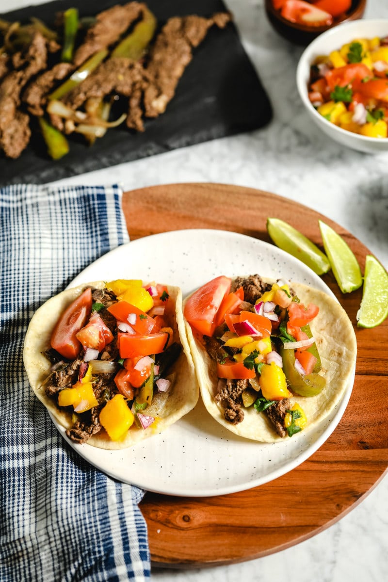 Beef Fajtas with mango salsa in two flour tortillas on a white plate with lime 