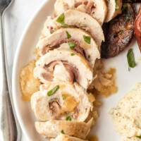 sliced chicken saltimbocca on a white plate with a fork on the side