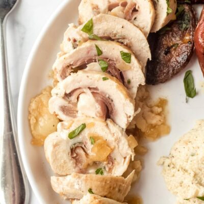 sliced chicken saltimbocca on a white plate with a fork on the side