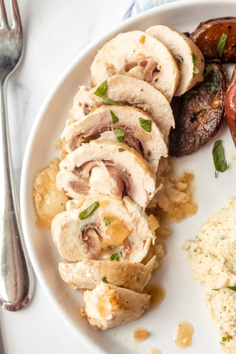 sliced chicken saltimbocca on a white plate with a fork on the side