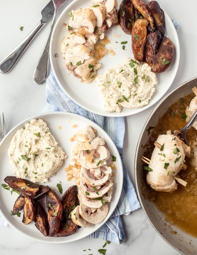 2 dinner plates with sliced chicken saltimbocca and side dishes on white plates with forks on side and pan of more chicken