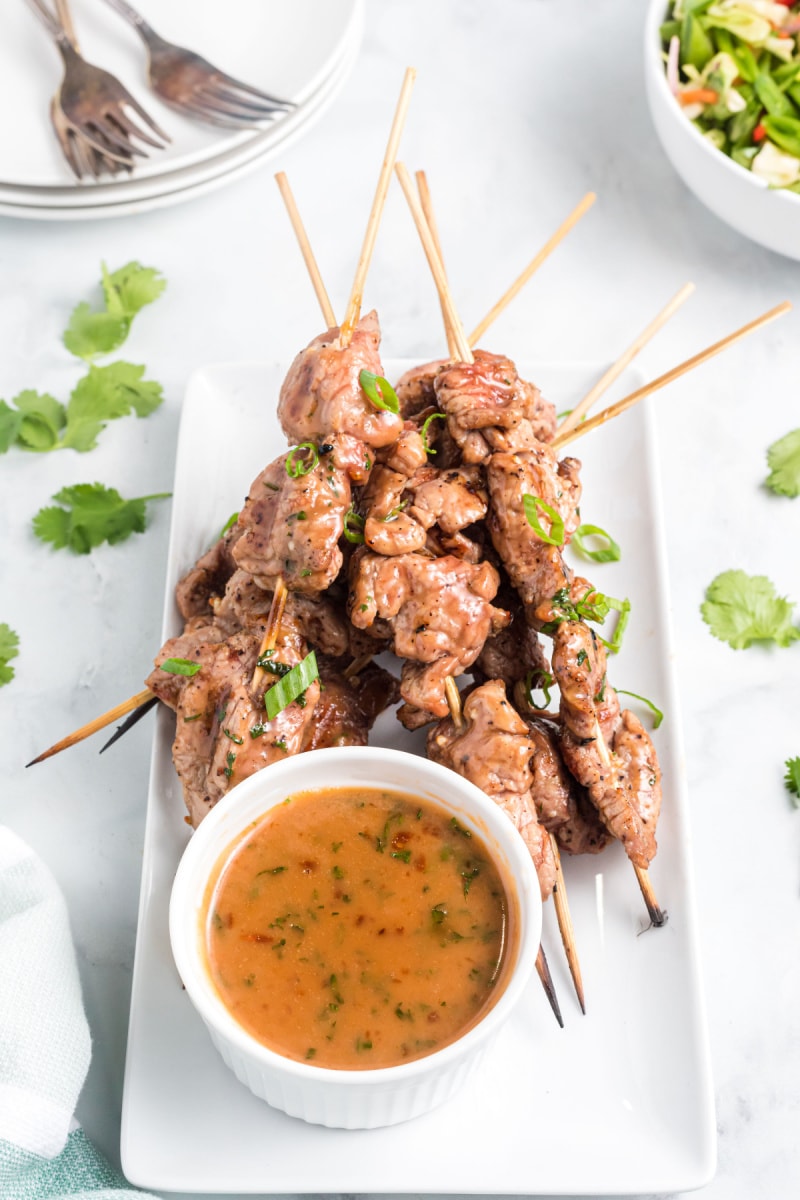 coconut curry pork satay on skewers on a platter with sauce
