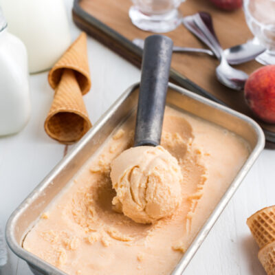 pan of fresh peach ice cream with scooper inside scooping a scoop