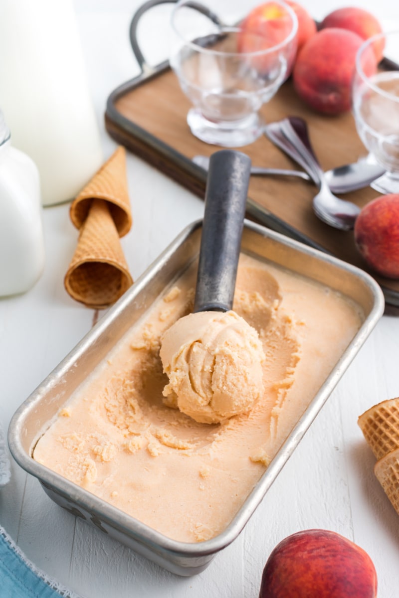 pan of fresh peach ice cream with scooper inside scooping a scoop