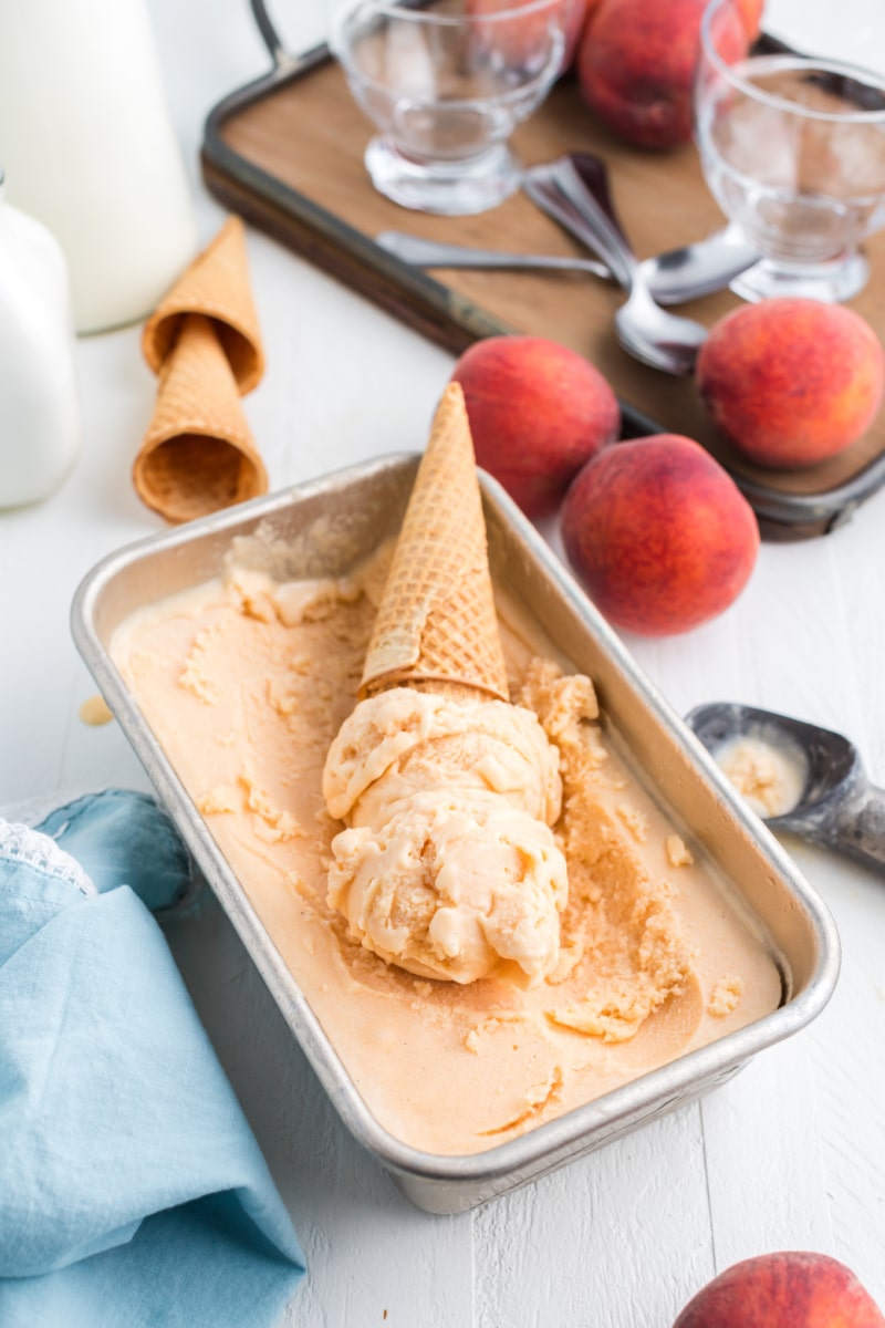 fresh peach ice cream in a dish with scoop and cone sitting on top