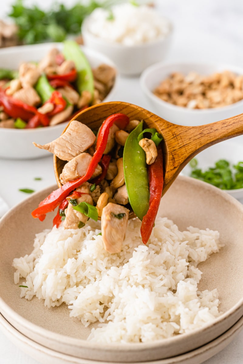 spooning garlic chicken stir fry onto bowl of rice