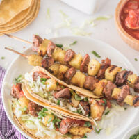 pork and pineapple soft tacos on a plate with kebabs on plate too