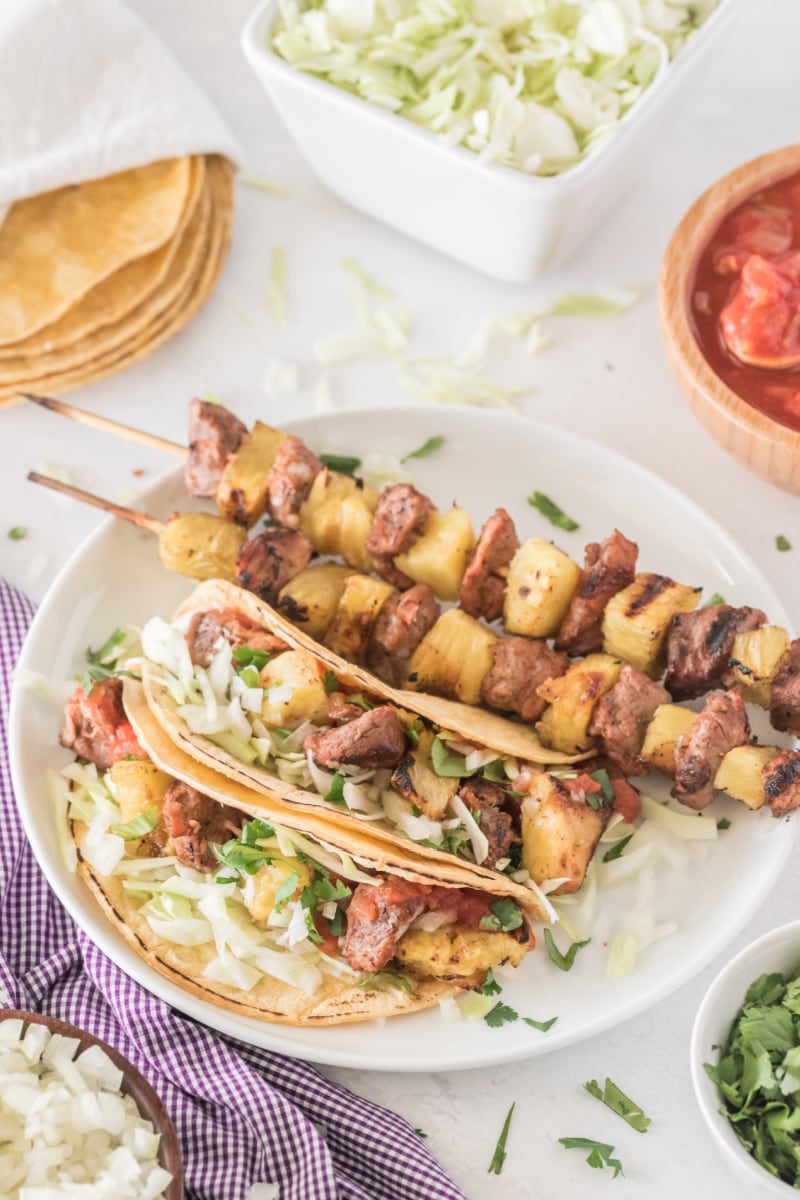 pork and pineapple soft tacos on a plate with kebabs on plate too