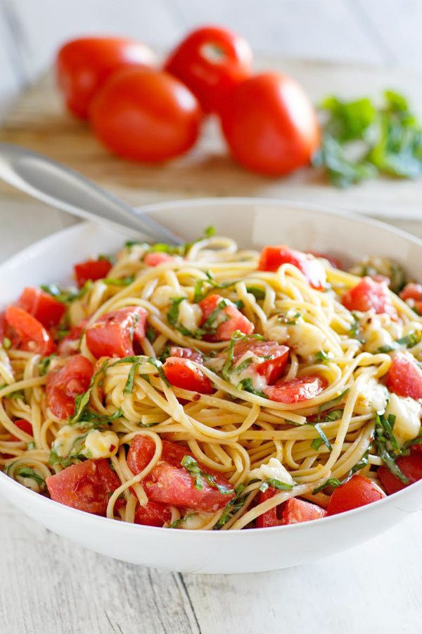 Linguine with Tomatoes Basil and Brie in a white bowl with a fork. fresh tomatoes and basil in the background