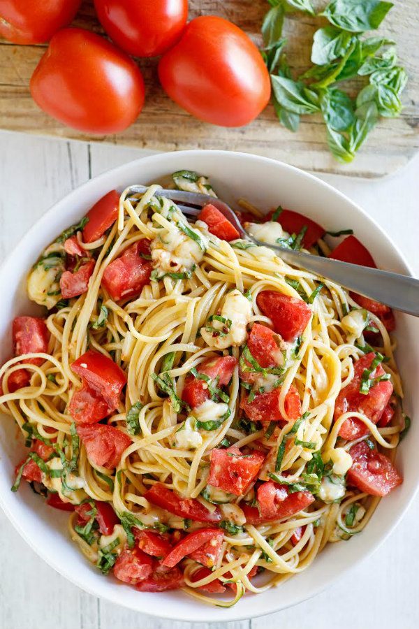 Linguine with Tomatoes Basil and Brie in a white bowl with a fork. fresh tomatoes and basil in the background