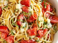 overhead shot of white bowl of linguine with tomatoes basil and brie with a fork