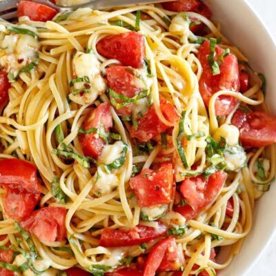 overhead shot of white bowl of linguine with tomatoes basil and brie with a fork
