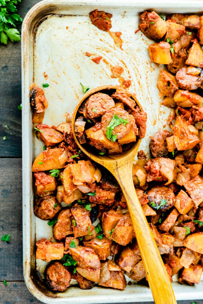 sheet pan of roasted portuguese potatoes and sausage showing wooden spoon serving