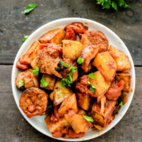 overhead shot of white bowl of portuguese roasted potatoes garnished with fresh parsley