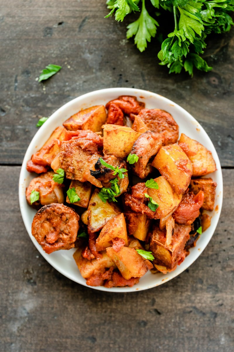 overhead shot of white bowl of portuguese roasted potatoes garnished with fresh parsley