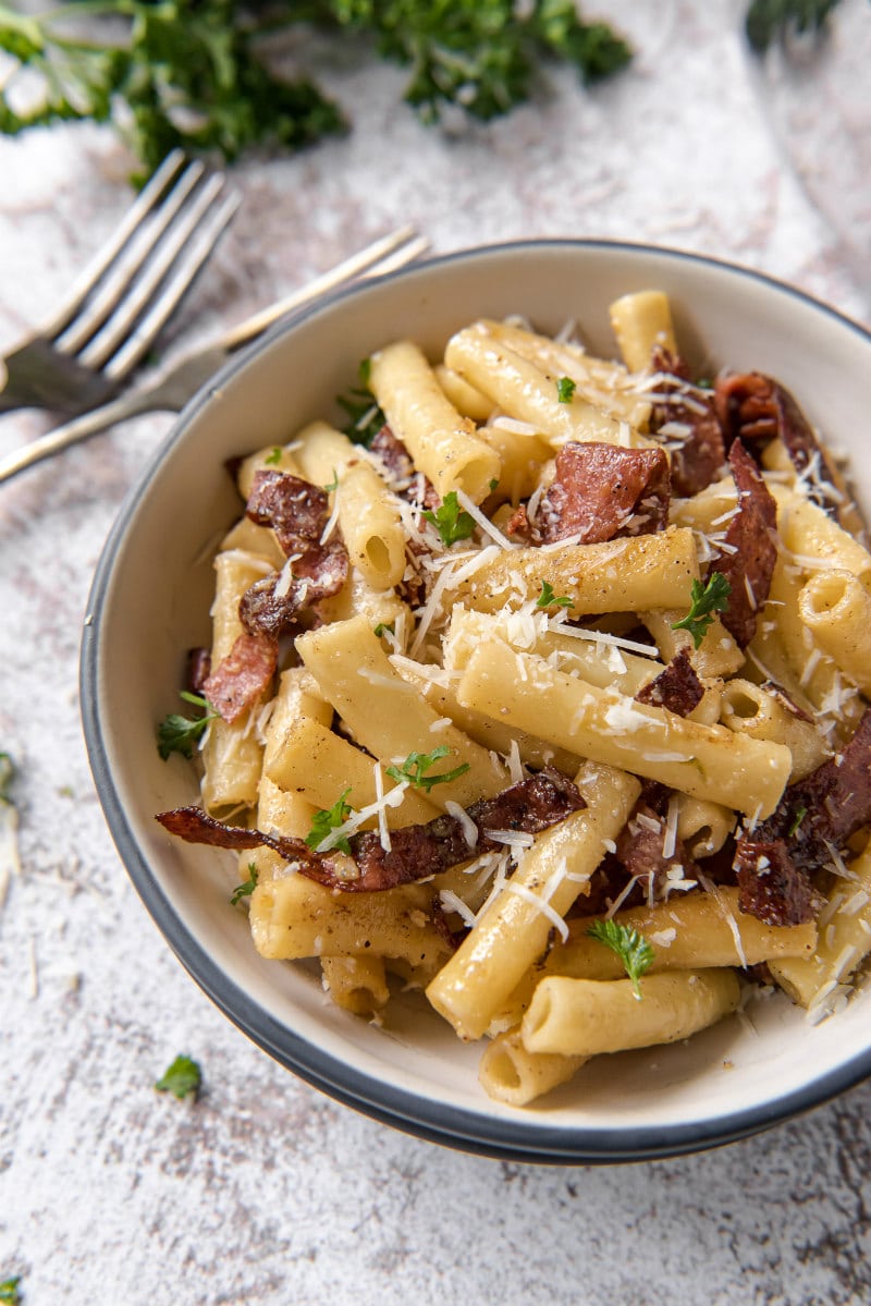 serving bowl of ziti carbonara with forks and fresh parsley on the side