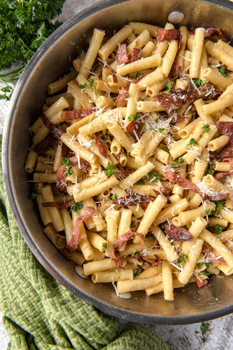 ziti carbonara in a skillet - green cloth napkin and fresh parsley on the side