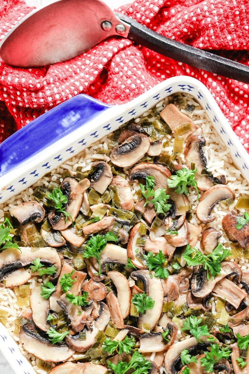 overhead shot of baked mushroom rice in a blue and white casserole dish with a red napkin and a serving spoon