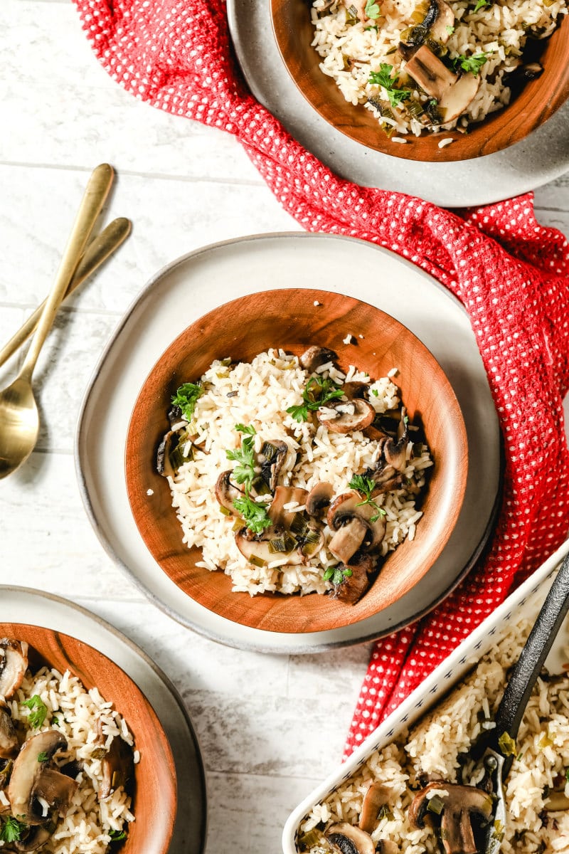 overhead shot of a serving of baked mushroom rice in a wooden bowl wit a red napkin and utensils