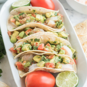 ceviche shrimp tacos displayed on a white platter with tomato and lime